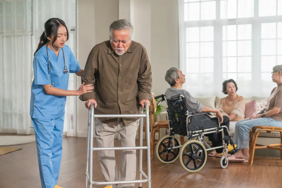 A nurse supporting an older man with a mobility frame in a senior-care facility